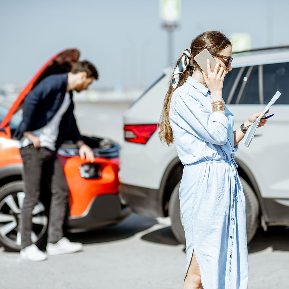 Woman calling road assistance or insurance company standing on the road after the car collision, man checking the damage