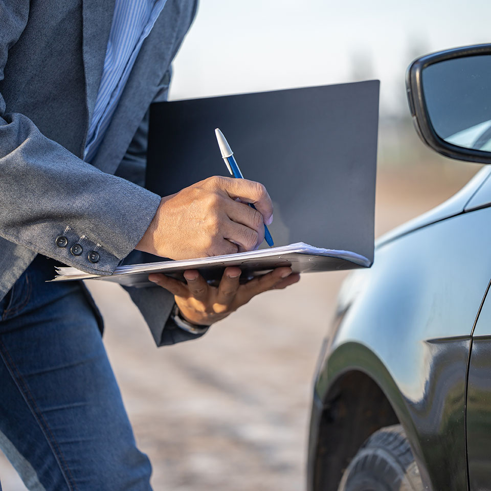 Insurance agent inspecting a car and taking notes.