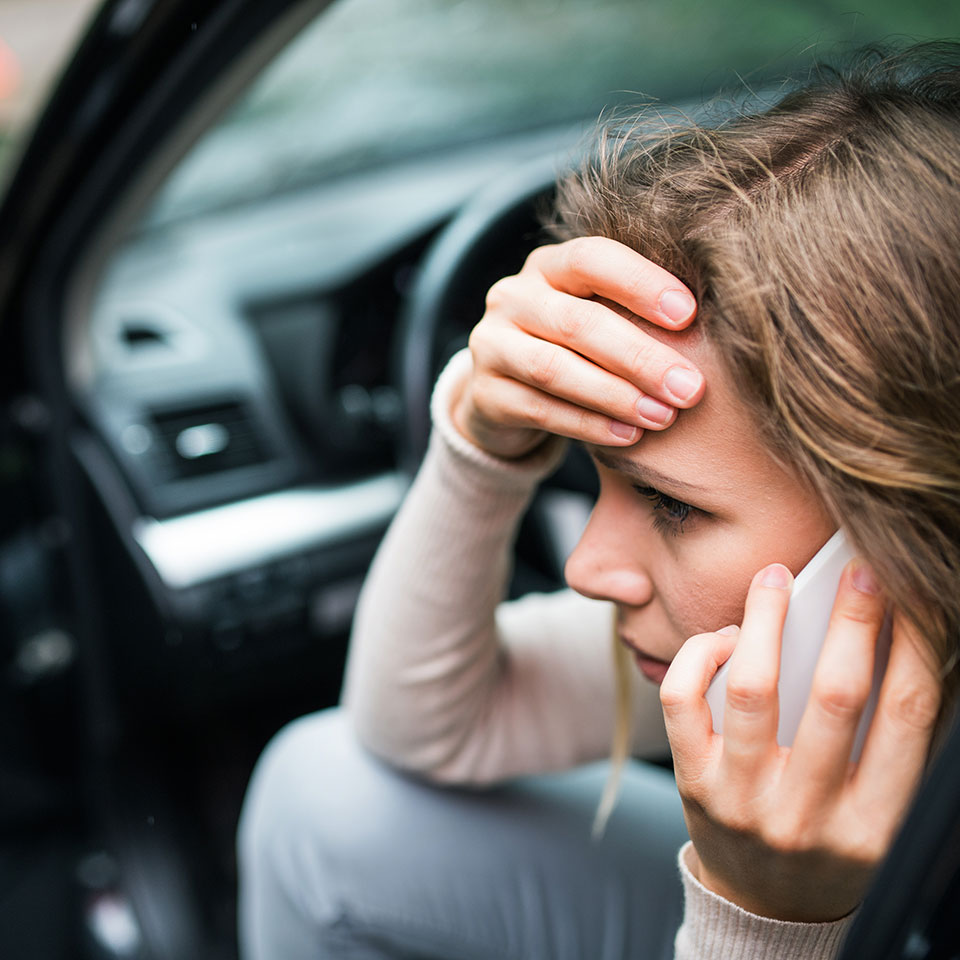 Young woman in the damaged car after a car accident, making a phone call.