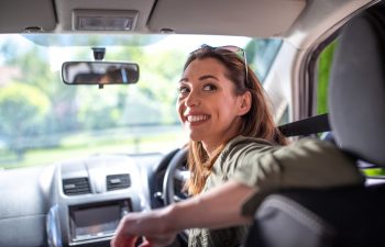 Pretty young woman driving car smiling. Attractive woman going in reverse looking back over shoulder.
